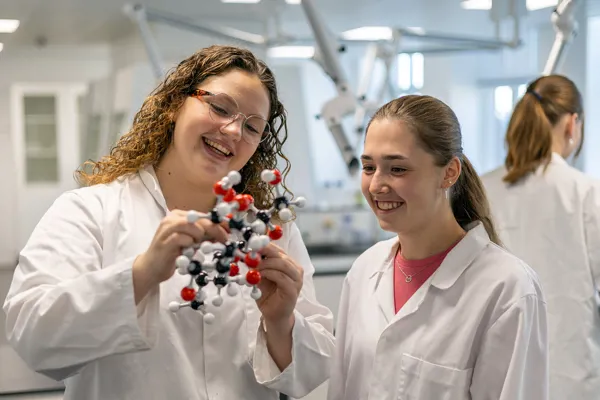 To smilende HTX piger i hvide kitler bygger molekyler